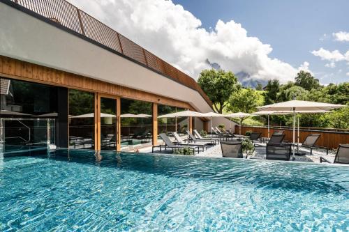 a swimming pool with chairs and umbrellas next to a building at Hotel Alpenroyal in Castelrotto