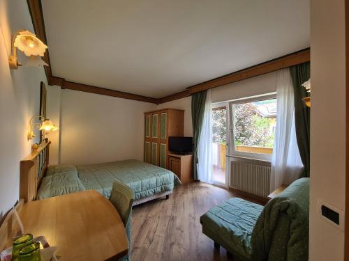 a bedroom with two beds and a table and a window at Alpenhotel Panorama in Campitello di Fassa