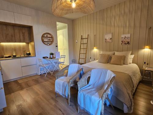 Cet appartement comprend une chambre avec un lit et deux chaises ainsi qu'une cuisine. dans l'établissement Arcarêve - Grand Studio Deluxe avec terrasse, jardin et accès plage, à Arcachon