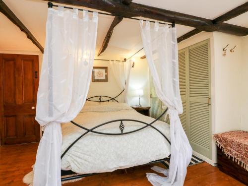 een slaapkamer met een hemelbed en witte gordijnen bij Westgate Cottage in Lapford