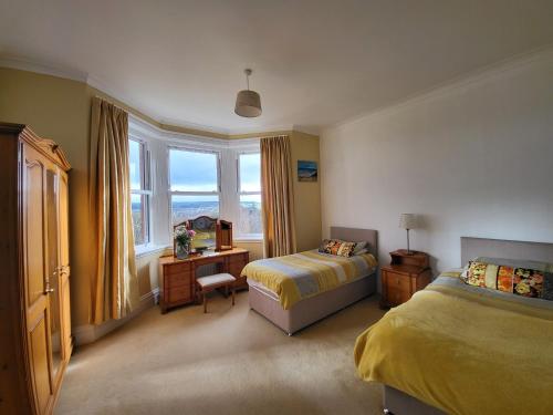 a bedroom with two beds and a desk and a window at Tan Tabin in Llandudno