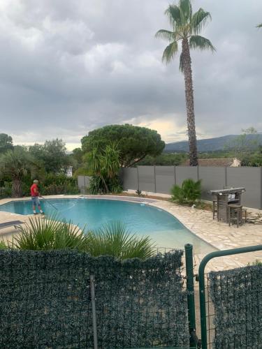 un homme debout à côté d'une piscine avec un palmier dans l'établissement Petit endroit paisible, à La Roquette-sur-Siagne