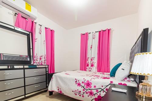 um quarto com cortinas cor-de-rosa, uma cama e um espelho. em Apartamento en ciudad Juan Bosh em Santo Domingo