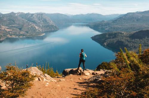 a person standing on top of a mountain overlooking a lake at El Refugio Ski & Summer Lodge in San Martín de los Andes