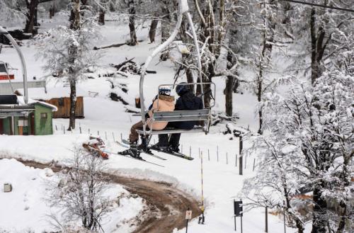 two people sitting on a ski lift in the snow at El Refugio Ski & Summer Lodge in San Martín de los Andes