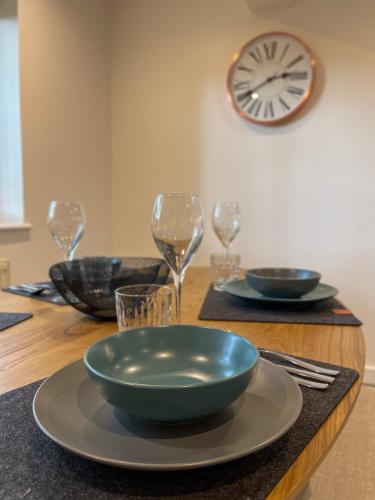 a wooden table with plates and glasses and a clock at Surrey Hills Lodge in Ewhurst