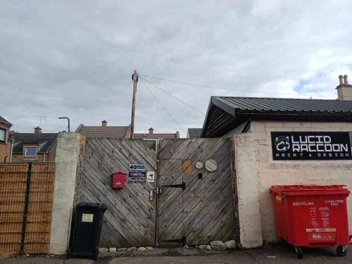uma cerca de madeira ao lado de um edifício com uma lata de lixo vermelha em The Lucid Racon em Inverness