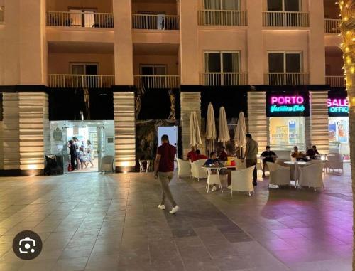 a person walking through a mall with tables and chairs at Port Golf Marina Families Only in El Alamein