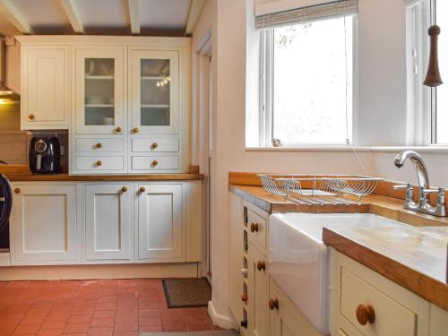 cocina con armarios blancos, fregadero y ventana en Penlan Cottage, en Cwrt-newydd