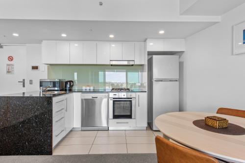 a kitchen with white cabinets and a table and a dining room at Proximity Waterfront Apartments in Redcliffe