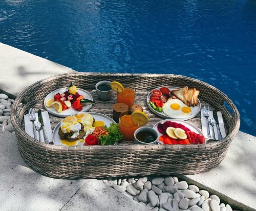 a table with breakfast food in a basket next to a pool at Villa Neshama in Canggu