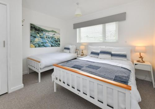 a white bedroom with two beds and a window at 20 Cae Du in Abersoch