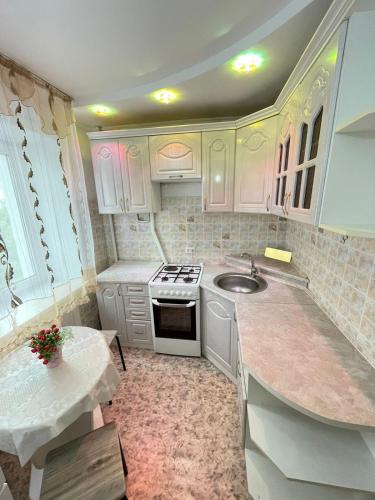 a kitchen with white cabinets and a sink and a stove at 1 комнатная квартира в центре in Petropavlovsk