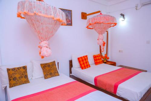 two beds in a room with red and orange pillows at Canal Side Guest House Polonnaruwa in Polonnaruwa