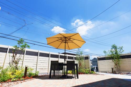 una mesa y dos sillas bajo una sombrilla amarilla en 新規オープン新築つくばガーデンハウス一棟貸切チャオ No361 en Tsukuba