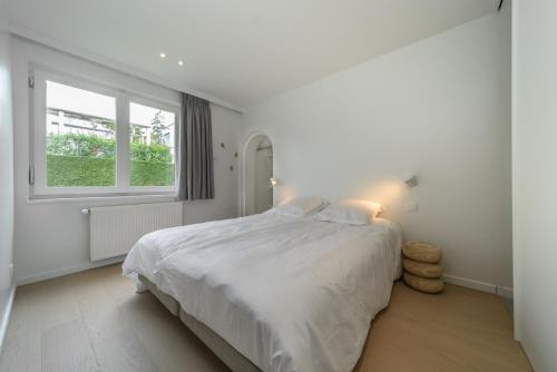 een witte slaapkamer met een groot bed en een raam bij Le Calme des Dunes in Koksijde