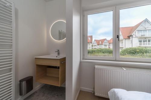 een badkamer met een wastafel en een raam bij Le Calme des Dunes in Koksijde
