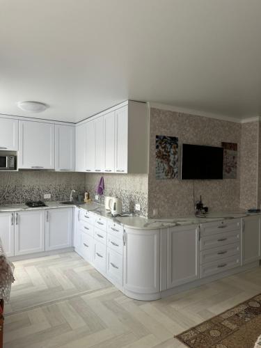 uma cozinha branca com armários brancos e uma televisão de ecrã plano em Квартира Уют em Borovoe