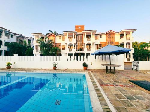 a swimming pool with a blue umbrella and some buildings at Selah Holiday Apartment at Sebuleni Nyali in Mombasa