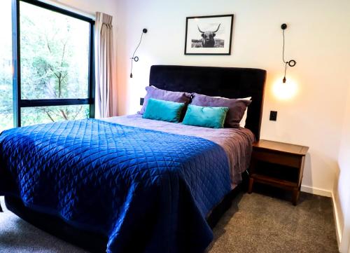 a bedroom with a bed with a blue comforter and a window at Black Barn Modern: Luxe Martinborough Escape in Martinborough 