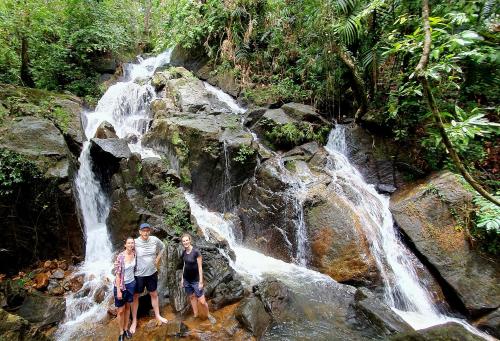 three people standing in front of a waterfall at Singharaja Garden AGRO ECO Lodge in Pelawatta
