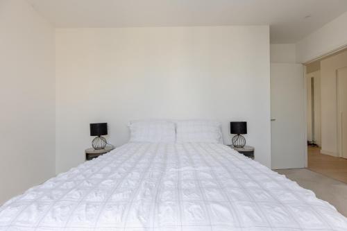 a white bed in a white bedroom with two lamps at Dockside Apartment With Scenic Views in London