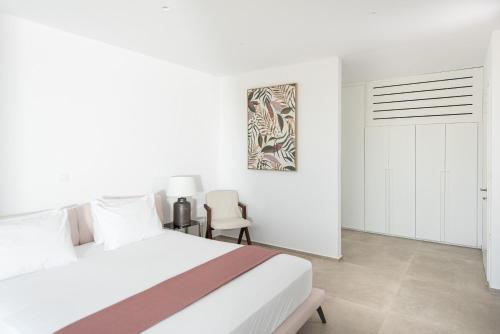 a white bedroom with a bed and a chair at Villa Inati in Nípos
