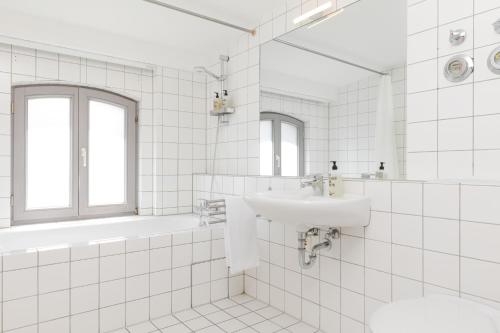 ein weiß gefliestes Bad mit einem Waschbecken und einer Badewanne in der Unterkunft Josty Brauerei Appartements in Berlin