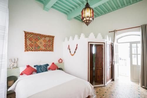 una camera con letto bianco e lampadario pendente di Riad l'Ayel d'Essaouira a Essaouira