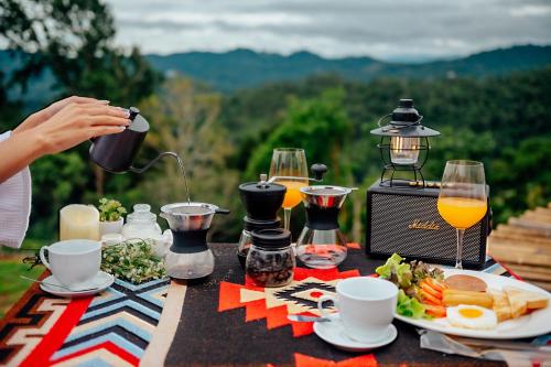 a picnic table with food and a person pouring orange juice at เดอะเนเจอร์ ม่อนแจ่ม The nature camping monjam in Mon Jam