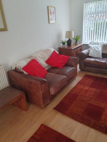 sala de estar con sofá marrón y almohadas rojas en Quiet house 8 mins from NEC/AIRPORT en Marston Green