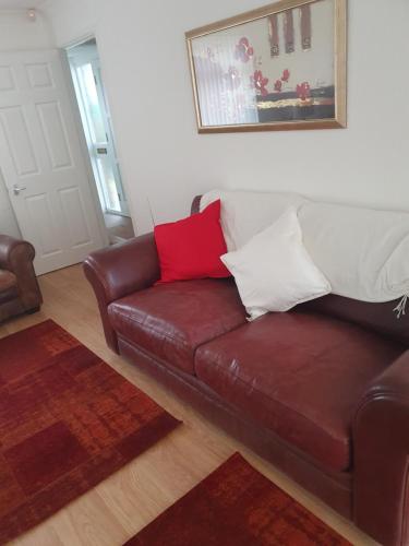 a living room with a brown leather couch with red and white pillows at Quiet house 8 mins from NEC/AIRPORT in Marston Green