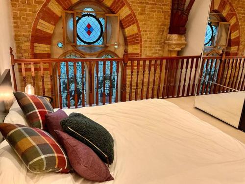 Magical Church Conversion in Watford في واتفورد: غرفة نوم مع سرير مع الوسائد ونافذة زجاجية ملطخة