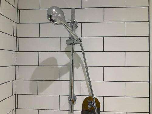 a shower head on a white tiled wall at Cosy Cottage at Duchess Farms in Sawbridgeworth
