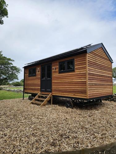a wooden tiny house sitting on top of a field at Woodland Shephards Hut - 'Aristocrat' in Caernarfon