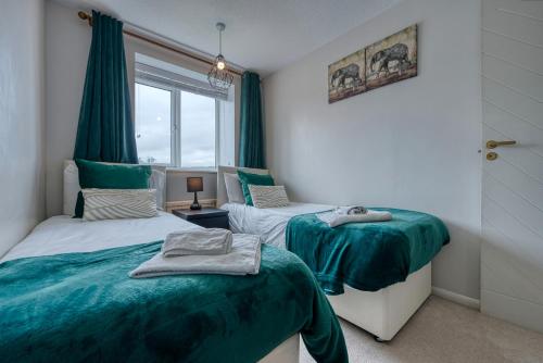 Duas camas num quarto com cortinas verdes e uma janela em CAPRI 13 SA - 3 bed House, Close to Loughborough University & M1 motorway, Free Wifi, Big garden, Ample parking- Ask for contractor rates! em Loughborough