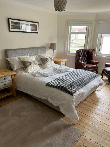 a bedroom with a bed and a chair and two windows at Loch Lomond Apartment in Alexandria