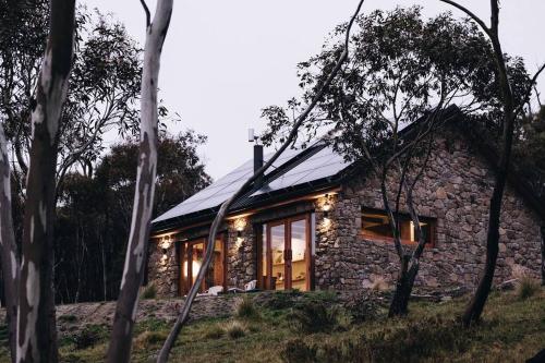 a stone house with lights on it in the woods at Mill Cabin —Luxury Granite Cabin, Mountain views in Crackenback