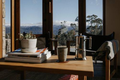 a table with books and a plant on it with a window at Mill Cabin —Luxury Granite Cabin, Mountain views in Crackenback