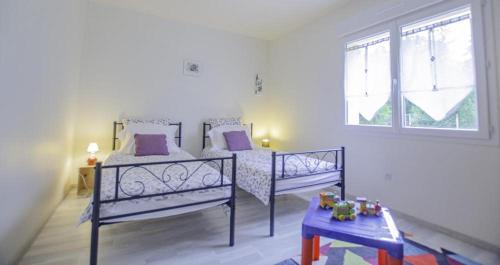 1 dormitorio con 2 camas con almohadas moradas y mesa en La petite maison rose, en Saint-Mards-en-Othe