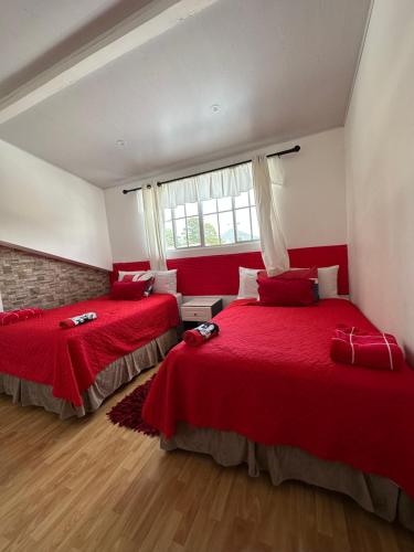 two beds in a room with red sheets and a window at La casa de luz in Concepción de Ataco