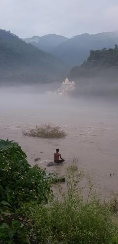 a man sitting in the water on a beach at Tebaar Backpackers in Rishīkesh