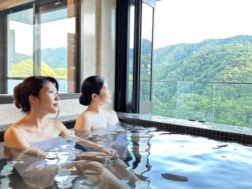 Dos mujeres sentadas en una bañera de hidromasaje con vistas en Garland Court Usami Private Hot Spring Condominium Hotel, en Ito