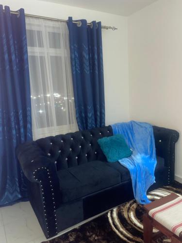 a black couch in a room with blue curtains at Omuts one bed airbnb with swimmingpool in Kiambu