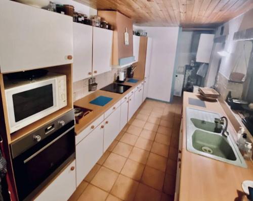 uma cozinha com armários brancos, um lavatório e um micro-ondas em Longère normande, parc, piscine. em Montchevrel