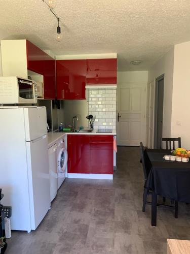 a kitchen with red cabinets and a white refrigerator at Appartement Cosy Tout Confort PARKING AC WIFI LINEN GARDEN INCLUDED complex access extra in Canet-en-Roussillon