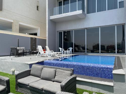 a swimming pool with a couch and chairs next to a house at Sama Chalet kuwait in Al Khīrān