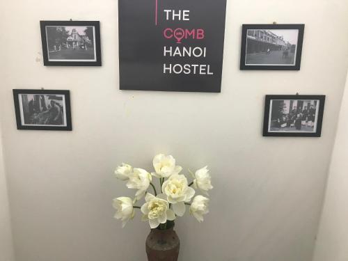 a vase with white flowers on a wall with pictures at The Comb Hanoi Hostel in Hanoi