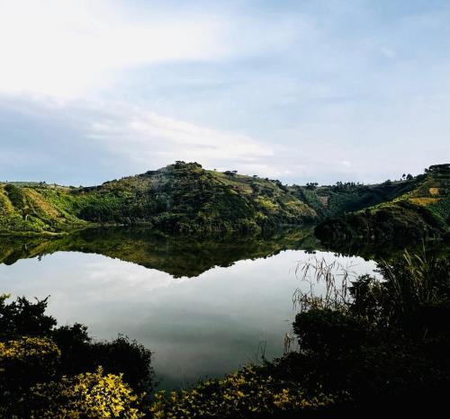 a lake in the middle of a hill with trees at Mwamba Kelele Lodge in Fort Portal