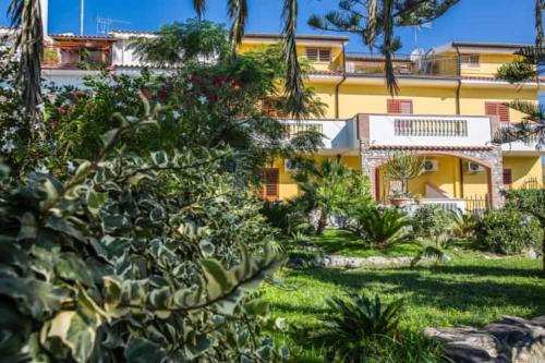 una casa gialla con alberi e piante di fronte di Casa Cosmano a Brancaleone Marina